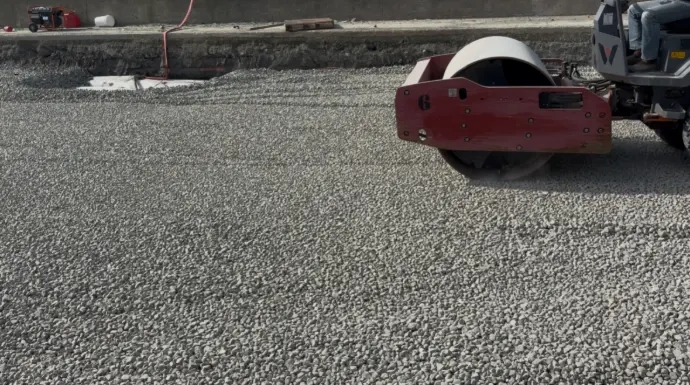 Roller compacting a layer of grey foam glass aggregate on a roadway fill